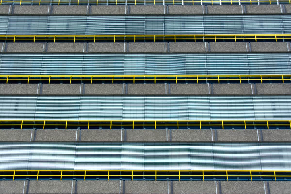 A gray concrete facade with repeating rows of caution-yellow railings
