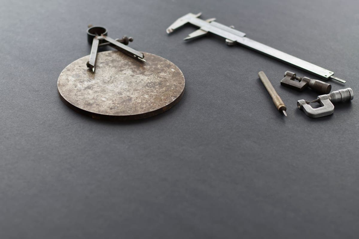 Precision measuring instruments — calipers, a micrometer and a compass — laid out on a dark gray surface